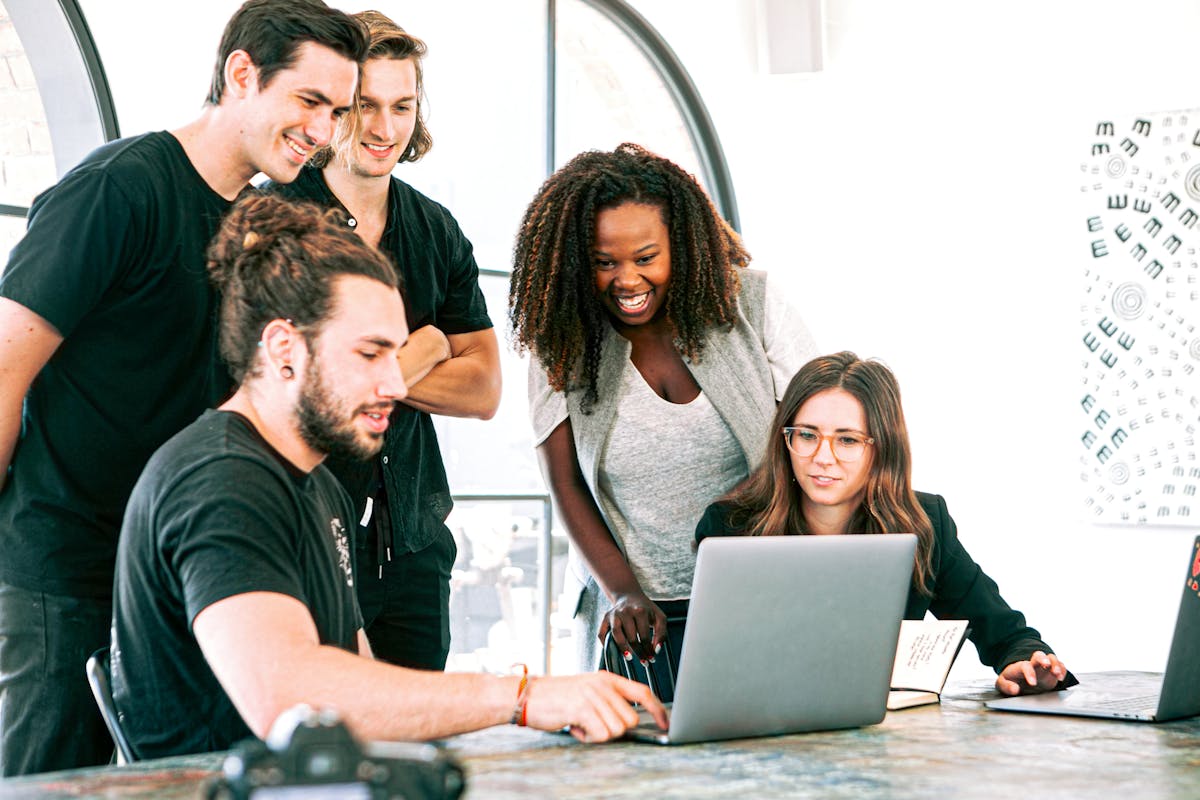 an employee working on a laptop while his colleagues are watching