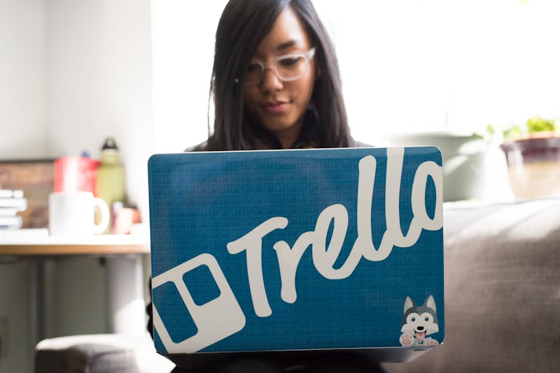 a woman working on a laptop with a Trello sticker